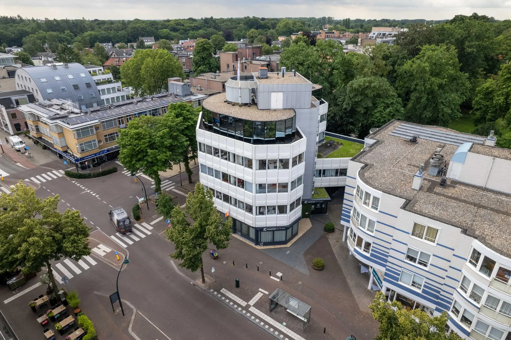 Luchtfoto van het kantoorgebouw aan de 1e Hogeweg in Zeist, omringd door bomen en stedelijke bebouwing.
